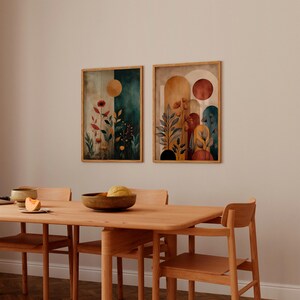 Puede incluir: Dos impresiones art&iacute;sticas bot&aacute;nicas enmarcadas con un estilo de acuarela. Una impresi&oacute;n presenta un fondo verde oscuro y beige con un sol dorado y flores rojas. La otra impresi&oacute;n tiene un fondo beige y naranja con un sol rojo y plantas estilizadas.