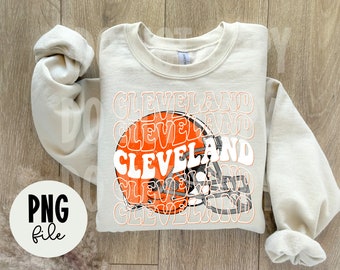 Puede incluir: Una sudadera beige con un diseño gráfico de un casco de fútbol y la palabra "Cleveland" repetida en una fuente retro.
