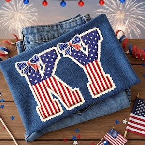 May include: Denim shirt with a patriotic "KY" design. The letters feature a red and white striped pattern and a blue background with white stars. The design is accented with a bow. American flags and festive decorations complete the scene.