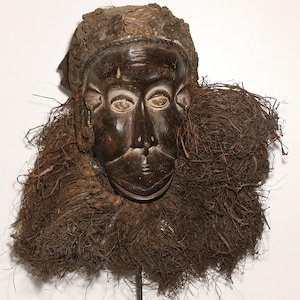 May include: A white ceramic mug with a black handle and the text "But First, Coffee" in a bold, black font. The mug is set against a blurred background, suggesting a cozy setting.