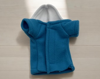 Pode incluir: Uma jaqueta de lã azul com capuz e forro branco. A jaqueta tem um zíper e mangas curtas.