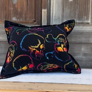 May include: A black pillow with a rainbow skull pattern. The skulls are outlined in black and filled with a rainbow gradient.