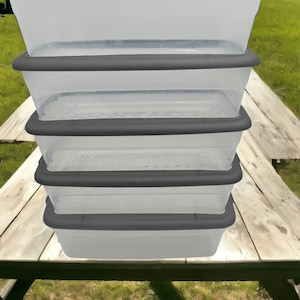 May include: Four clear plastic storage bins with gray lids stacked on top of each other. The bins are sitting on a wooden surface.