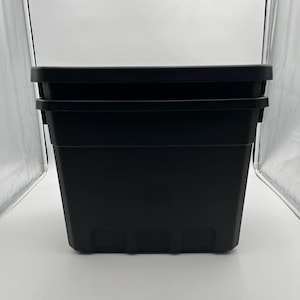 May include: A stack of two black plastic storage containers. The containers are rectangular with a slightly tapered design and a flat top. The containers are designed for storage.