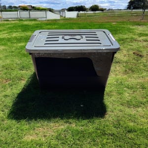 May include: A large, gray plastic storage bin with a lid. The bin has a rectangular shape and a textured surface. The lid has a built-in handle and a small, rectangular opening.