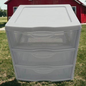 May include: A white plastic three-drawer organizer with clear drawers. The drawers have a grid pattern.
