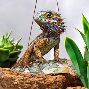 May include: A colorful, mosaic-style lizard figurine with a bright blue and purple head and orange and yellow body. The lizard is perched on a rock with a mosaic design.