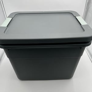 May include: A dark gray storage bin with a matching lid. The lid has two light gray rectangular accents. The bin is made of plastic and is designed for organizing and storing items. The bin is square-shaped.