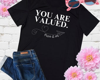 May include: Black t-shirt with white text that reads "YOU ARE VALUED. Pass it on."  A paper airplane with a heart is drawn next to the text.