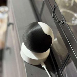 May include: A modern, two-toned decorative sphere, split between black and white, sits atop a white, tiered base. The sphere has a textured surface, and a white cable extends from the base. The design is minimalist and contemporary.