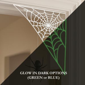K&ouml;nnte beinhalten: Wei&szlig;e Spinnennetzdekoration mit einer schwarzen Spinne, die darunter h&auml;ngt. Das Netz ist dreieckig und passt in eine Ecke. Der Text "GLOW IN DARK OPTIONS (GREEN or BLUE)" befindet sich unten. Das Netz leuchtet im Dunkeln gr&uuml;n.