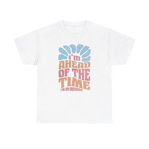 Puede incluir: Camiseta blanca con un gráfico de estilo retro que dice "I'm Ahead of the Time I'm an Aquarius" en un arcoíris de colores.
