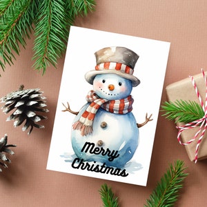 Puede incluir: Una ilustraci&oacute;n de acuarela de un mu&ntilde;eco de nieve con una bufanda a rayas rojas y blancas y un sombrero de copa marr&oacute;n. El mu&ntilde;eco de nieve est&aacute; de pie sobre un fondo blanco con el texto "Merry Christmas" escrito debajo.