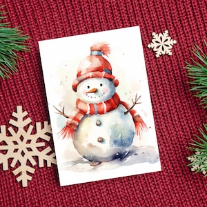 Puede incluir: Una pintura de acuarela de un mu&ntilde;eco de nieve con un sombrero y una bufanda rojos y blancos. El mu&ntilde;eco de nieve est&aacute; de pie sobre un fondo blanco con un cielo azul claro.