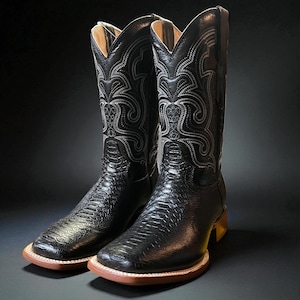 May include: A pair of black cowboy boots with a square toe and decorative stitching. The boots have a textured pattern on the vamp and shaft, with a light brown sole and heel. The interior is a light tan colour.