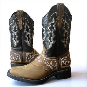 May include: A pair of cowboy boots with a square toe. The boots feature a brown and black leather design with white decorative stitching. The shaft is black with brown accents, and the foot is tan. The boots have a classic Western style.