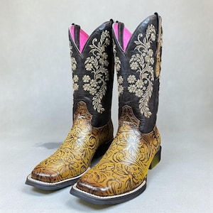 May include: A pair of brown and tan cowboy boots with floral embroidery and tooling. The boots have a square toe, a pink interior, and a black sole. The shaft is approximately 30 cm tall.