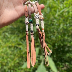 May include: A collection of four leather horse reins with braided white and brown accents. Each rein features a different design, including green and black beads, and ends with long, tan leather fringe.