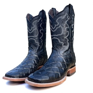 May include: A pair of black cowboy boots with a square toe and a textured, crocodile-like pattern. The boots have decorative white stitching and a light brown sole. The shaft of the boots is tall, and the leather appears to be glossy.
