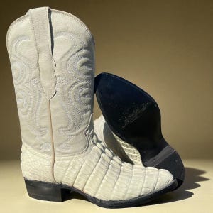 Könnte beinhalten: Off-white Cowboy-Stiefel mit strukturiertem, gemustertem Design. Die Stiefel haben eine spitze Zehenpartie und einen gestapelten Absatz. Die Sohle des Stiefels ist schwarz. Der Schaft des Stiefels weist dekorative Nähte auf.