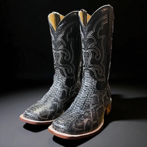 May include: A pair of black cowboy boots featuring a snakeskin pattern on the foot and decorative stitching on the shaft. The boots have a square toe and a brown sole, set against a dark backdrop.