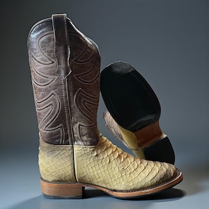 May include: Cowboy boots in a two-tone design. The upper shaft is brown leather with decorative stitching, while the lower part has a textured, light-coloured pattern. The soles are brown with a black rubber heel.