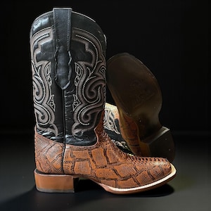 May include: A pair of cowboy boots. The boots have a black shaft with white decorative stitching. The lower part of the boot is brown with a reptile-like texture. The boots have a square toe and a stacked heel, against a dark background.