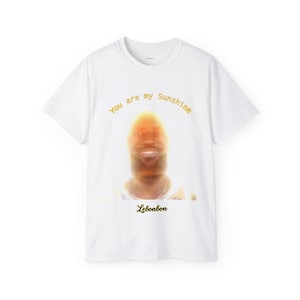 May include: White t-shirt with a blurred image of a person's face and the text "You are my Sunshine" in yellow. The text "Lebonbon" is printed in yellow at the bottom of the shirt.