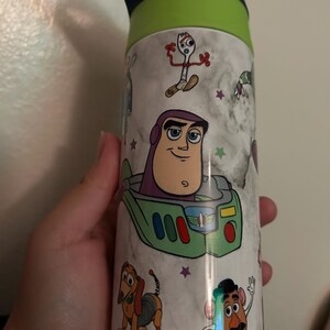 May include: A stainless steel water bottle featuring characters from the animated film Toy Story. The bottle has a white marble-like background with images of Buzz Lightyear, Forky, Slinky Dog, and Mr. Potato Head. The lid is green and blue.