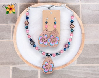 Peut inclure: Un collier et des boucles d'oreilles assortis en bois avec un motif de fleur d'hibiscus rose et bleu. Le collier est composé de perles et de bois, et les boucles d'oreilles sont en forme de goutte d'eau en bois avec un motif de fleur d'hibiscus rose et bleu.