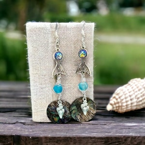 May include: A pair of silver mermaid tail earrings with iridescent blue and green stones, blue glass beads, and abalone shell accents.