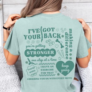 May include: Teal blue t-shirt with a graphic print of a spine, dumbbells, a bone, and a heart. The text on the shirt reads "I've got your back* you're getting stronger one step at a time you're doing gait! I have an exercise for that keep going cheering you on with every move making a difference".