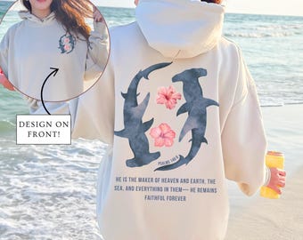 May include: A cream-colored hoodie with a design on the back featuring two hammerhead sharks and pink flowers. The text "PSALMS 146:6" and "HE IS THE MAKER OF HEAVEN AND EARTH, THE SEA, AND EVERYTHING IN THEM - HE REMAINS FAITHFUL FOREVER" is printed on the hoodie.