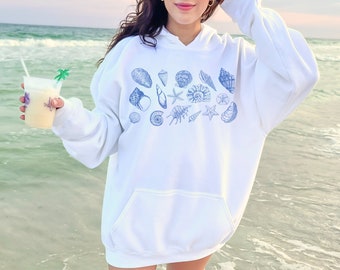 May include: White hoodie with a blue seashell print. The hoodie has a drawstring hood and a kangaroo pocket.