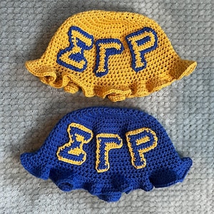 Könnte beinhalten: Zwei gehäkelte Bucket-Hats, einer gelb und einer blau, mit den Buchstaben "BFP" in einer kontrastierenden Farbe auf jedem Hut.