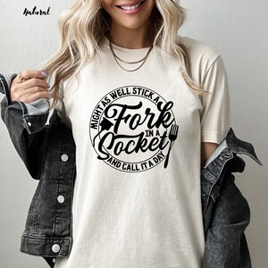 May include: A white t-shirt with a black circle graphic that says "Might as well stick a fork in a socket and call it a day".