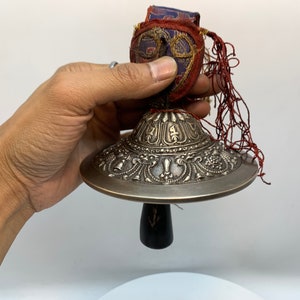 Tibetansk bonpoklocka, klocka i antik finish. Handgjord klocka i legering med hållare i antik tyg. Hornpendel att ringa.
