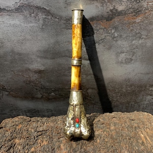 May include: A tall, slender, cylindrical object featuring a polished, light-brown, marbled-patterned shaft accented with silver-toned metal bands at the top, middle, and base. The flared base is decorated with intricate embossed patterns and two small, oval-shaped red and turquoise-colored stones.