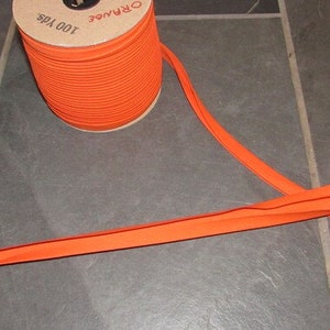 May include: A spool of 100 yards of orange bias tape. The tape is wound around a cardboard spool with the label "ORANGE 100 YDS".