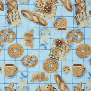 May include: A blue and white patterned fabric with a repeating pattern of various baked goods, including croissants, pretzels, bagels, cookies, and bread. There are also coffee cups and jars with a floral design.
