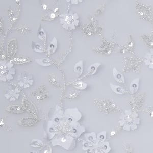 May include: White floral lace fabric with sequins. The fabric features a delicate floral pattern with small white flowers and leaves. The sequins are scattered throughout the fabric, adding a touch of sparkle.