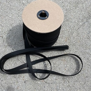 May include: A spool of black elastic band, wound around a cardboard core. The elastic is coiled and ready to be used for sewing or crafting projects.