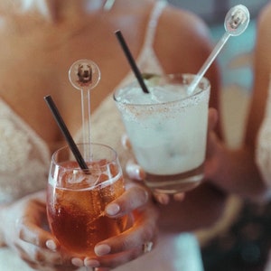 K&ouml;nnte beinhalten: Zwei Cocktails mit personalisierten Getr&auml;nke-R&uuml;hrst&auml;bchen mit Hundefotos. Der eine Cocktail ist hellorange und der andere ist klar, hellgelb.