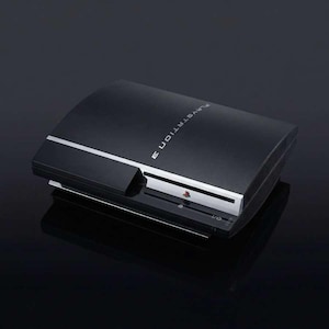 May include: A black PlayStation 3 console with a silver accent line. The console has the PlayStation 3 logo and the words "PlayStation 3" printed on the top. The console is on a black surface.