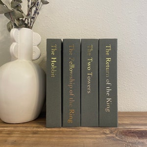 May include: Four hardcover books with gold lettering on a dark green background. The titles are "The Return of the King", "The Two Towers", "The Fellowship of the Ring", and "The Hobbit".
