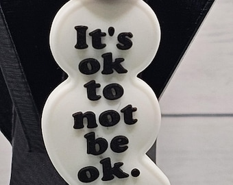 May include: White bead necklace with a white bead that says "It's ok to not be ok." The bead is attached to a colorful paisley patterned bead and a iridescent bead.