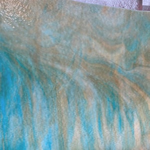 May include: A large, curved panel with a flowing, abstract design. The colors include shades of blue, tan, and white, creating a watery or cloud-like effect. The panel is set against a blurred outdoor background.