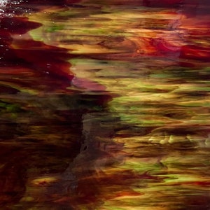 May include: A rectangular sheet of stained glass with a flowing, abstract design. The colors transition from deep reds and browns at the top to greens and yellows at the bottom, creating a landscape effect. The glass is displayed near a window.