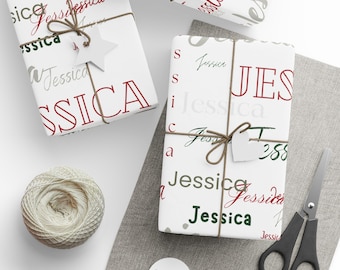 Puede incluir: Cajas de regalo blancas envueltas en papel con el nombre "Jessica" en rojo, verde y gris. Los regalos están atados con hilo y adornados con etiquetas en forma de estrella y corazón. También hay una madeja de hilo y unas tijeras.