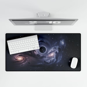 Puede incluir: Una alfombrilla de escritorio rectangular negra con un diseño de galaxia cósmica y un agujero negro central. Un teclado y un ratón blancos están sobre la alfombrilla. Un monitor de ordenador está encima.